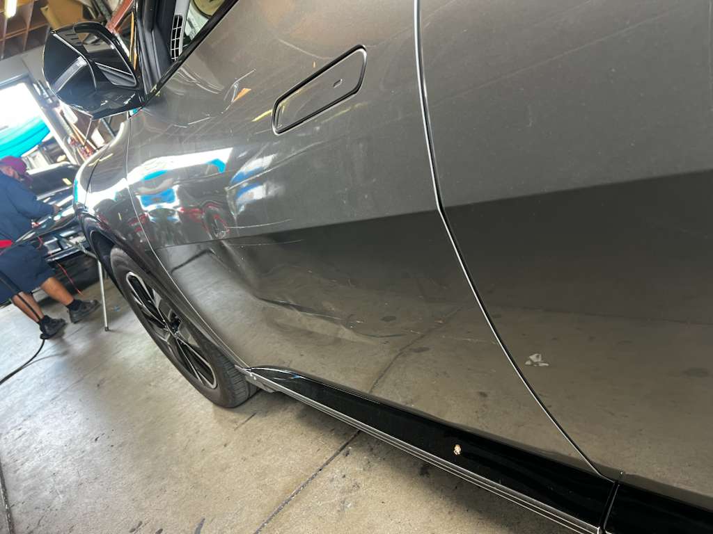 Body technician inspecting and repairing a deep dent on a luxury sedan door panel